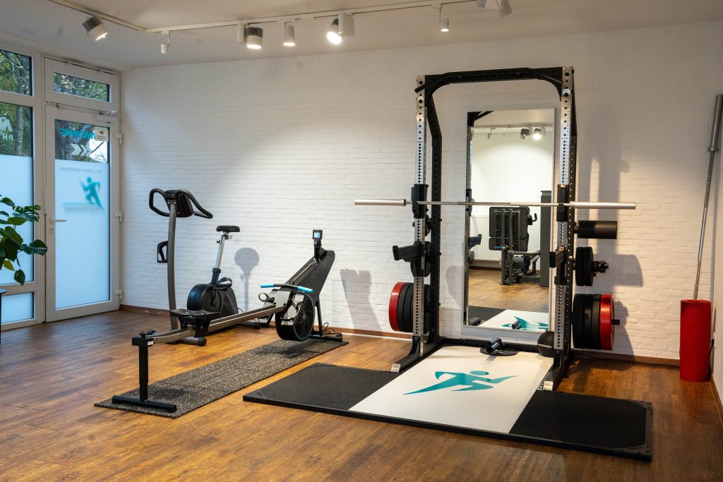 Das Fitnessstudio eines Physiotherapie-Zentrums mit einem Rudergerät und einem Squat Rack für funktionelles Training und Rehabilitation.