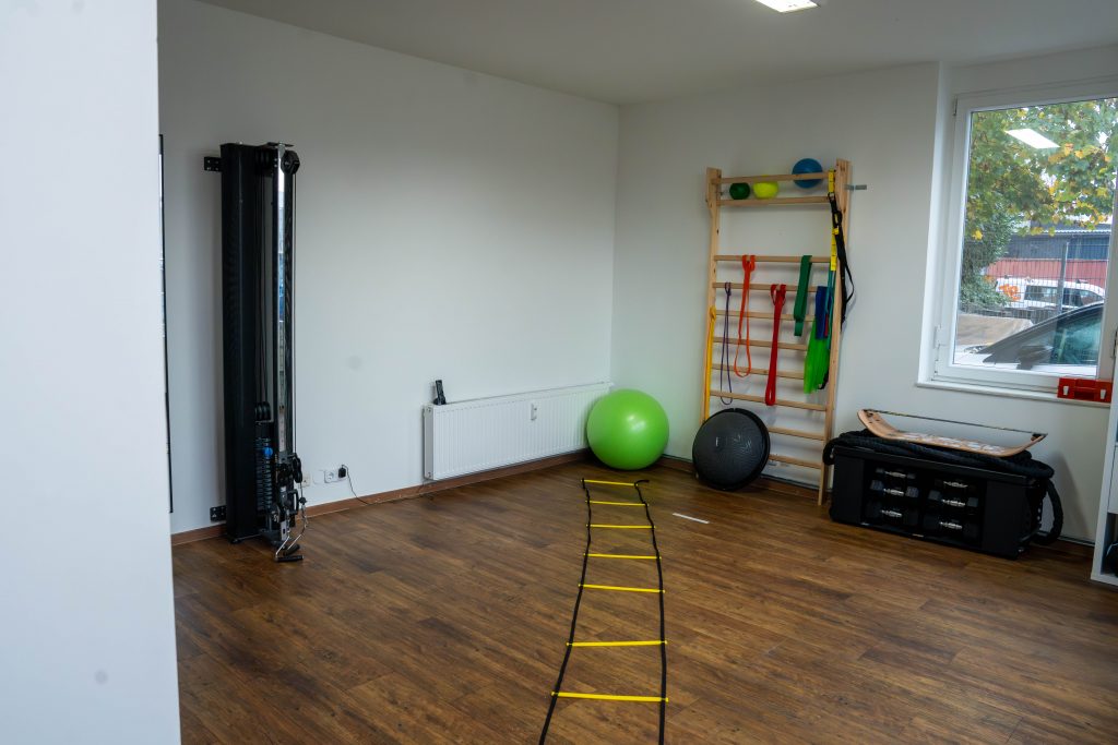 Eine moderne Trainingsfläche mit verschiedenen Fitnessgeräten und einer Wand mit Übungsbändern. Der Raum ist gut beleuchtet und bietet genügend Platz für individuelle Trainingseinheiten.