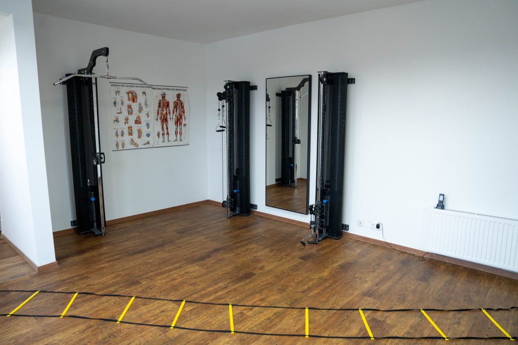 Ein Trainingsraum mit einem modernen Kabelzuggerät, Spiegeln und einer Trainingsleiter auf dem Boden. Es wird viel Platz für funktionelle Übungen geboten.